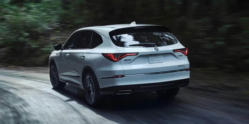 White Acura MDX driving on a forest road from rear angle